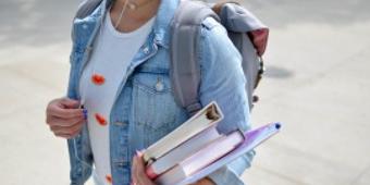 person with books in hand and a backpack on their back